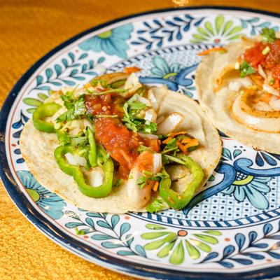 Vegetarian tacos topped with salsa, green peppers, and herbs.