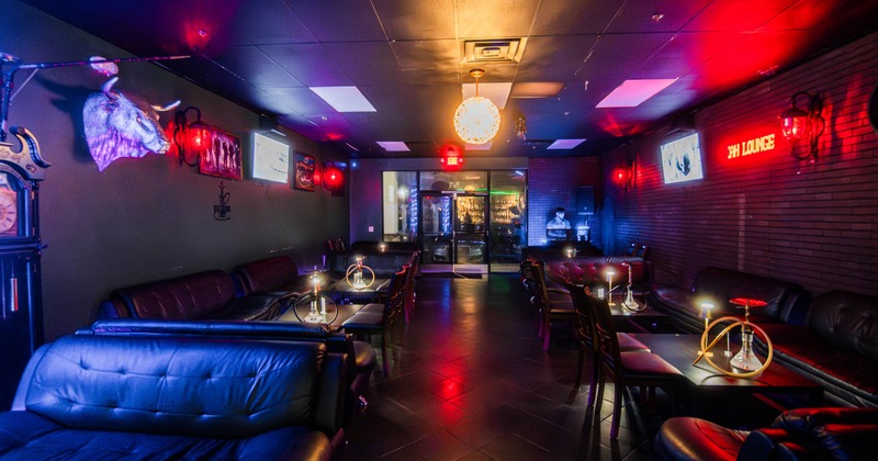 Interior, dimly lit lounge with leather couches, tables with hookahs, and a neon sign