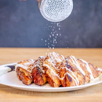 French Toast drizzled with vanilla buttercream, being dusted with powdered sugar.