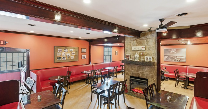 Interior with red booths, wooden chairs, a stone fireplace and orange walls.