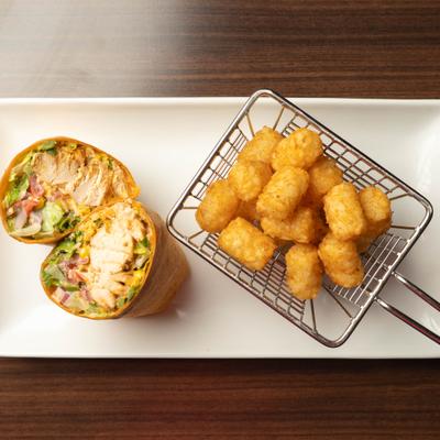 Top*down view of a halved chicken wrap served with tater tots.