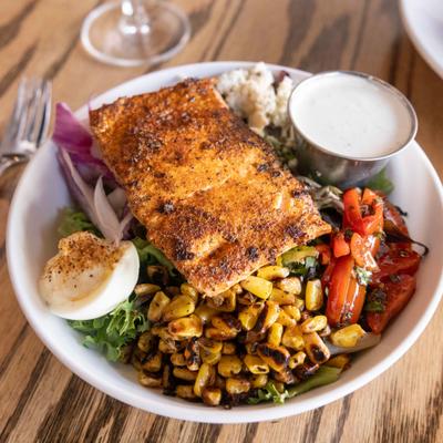 Grilled salmon served over a Cobb salad with corn, egg, greens, and blue cheese.