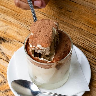 Spoon with a bite of tiramisu served in a glass.
