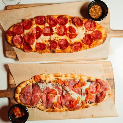 Two flatbreads, one with pepperoni, the other with salami and tomato, on wooden boards.