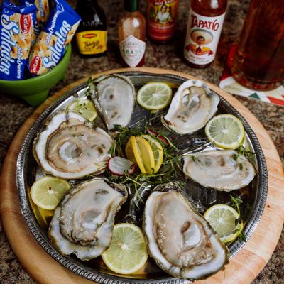 Platter of fresh raw oysters served on a metal tray with lemon slices and herbs.