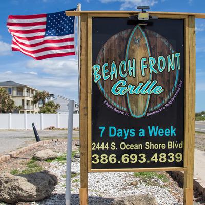 Restaurant outdoor signage featuring a surfboard, next to a American flag.