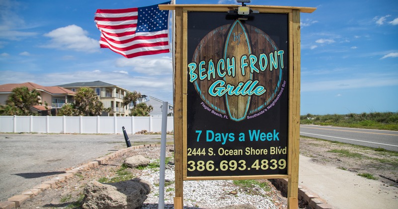 Restaurant outdoor signage featuring a surfboard, next to a American flag