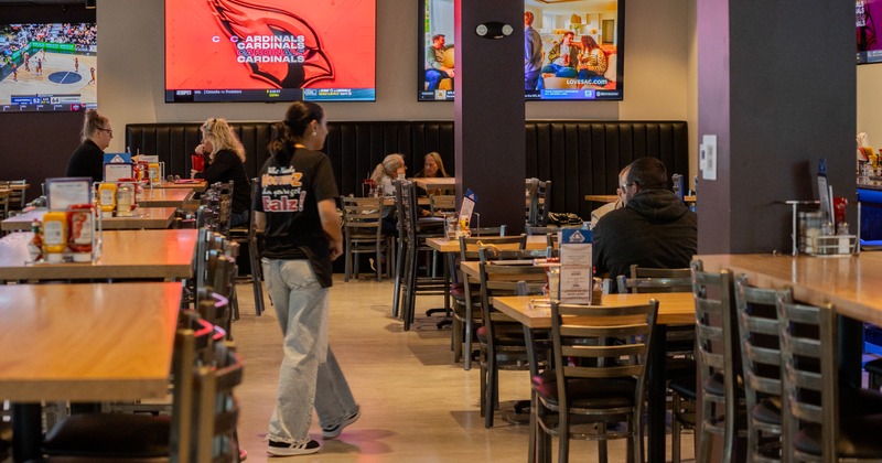 Diner area, tables and chairs, waitress brings the food, guests, tv screens above