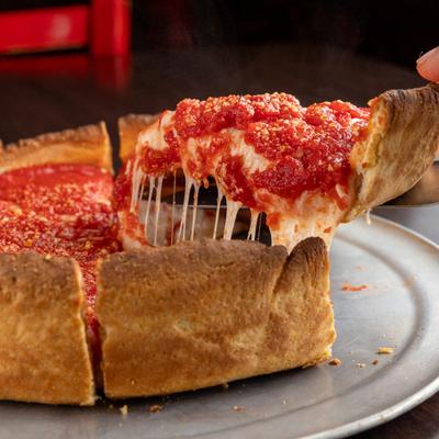 A hand grabbing a piece of the Chicago deep dish pizza.