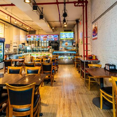 Cafe interior with wooden tables, chairs, display case, and digital menu boards.
