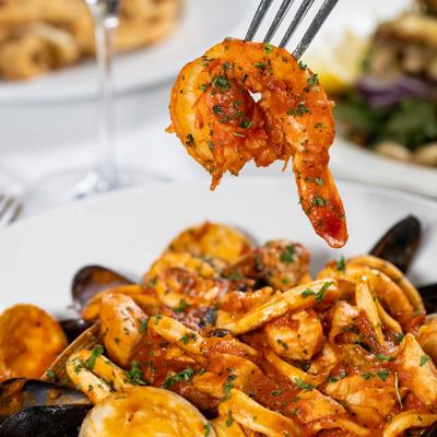 Fork holding a seasoned shrimp over a plate of seafood pasta.