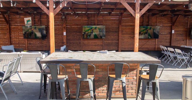Outdoor seating area with a stone table and metal stools under a wooden pergola