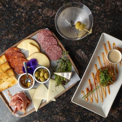 Charcuterie board, crab cake plate, and martini on dark countertop.