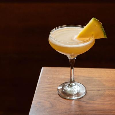 A yellow cocktail glass garnished with a pineapple wedge.