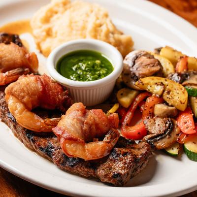Grilled steak topped with shrimp, served with grilled vegetables, green salsa, and mashed potato.