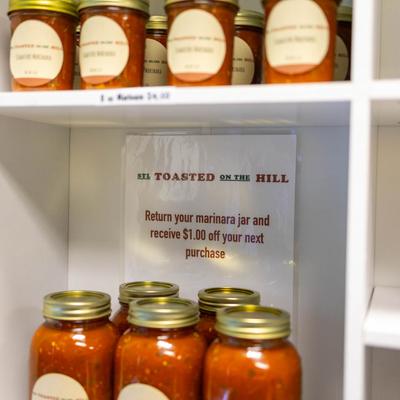 Jars of marinara sauce on white shelves with a promotional sign.