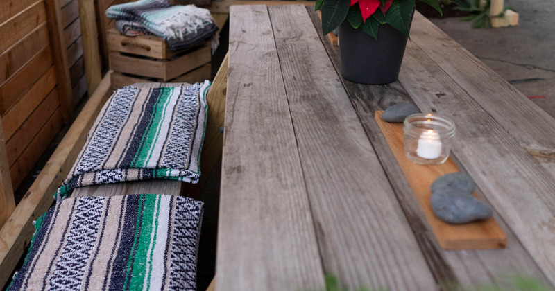 Picnic table with a pointsettia, a burning candle and multi colored blankets on the benches