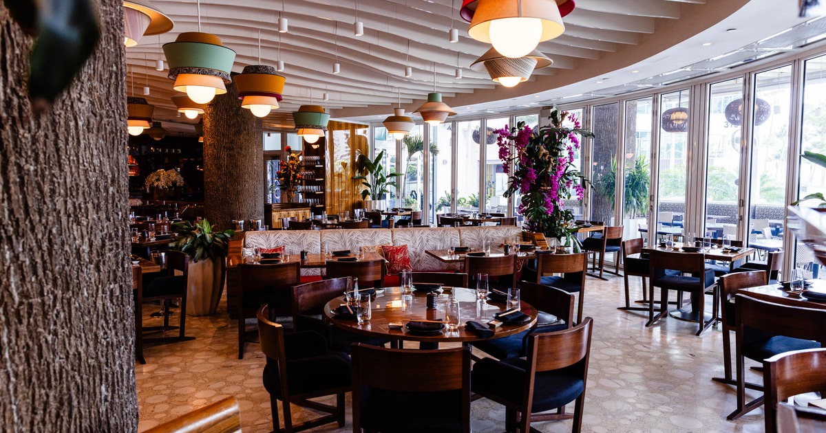 A modern interior - round wooden tables with chairs, colorful pendant lights, floral decorations
