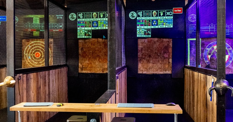 Axe-throwing venue with targets, digital scoreboards, and a table with stools