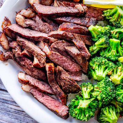 Slices of grilled sirloin steak are served next to steamed broccoli on a white plate.