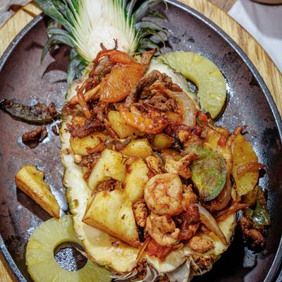 Hawaiian Fajita with steak, shrimp, and chicken served inside a hollowed-out pineapple half.
