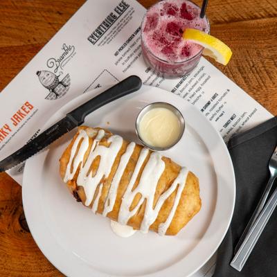 Chimichanga covered in cheese sauce, with dipping sauce and a cocktail drink.
