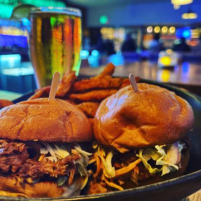 Two pulled pork sliders with fries and beer in a bar setting.
