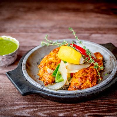 Spiced chicken garnished with lemon, onions, bell peppers, and thyme, served with green chutney.