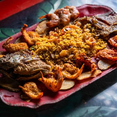 Seafood platter featuring a central mound of rice, whole fried fish, shrimp and plantains.