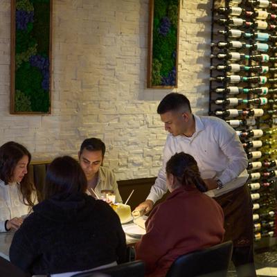 Server attending diners at a table beside a wall of wine bottles.
