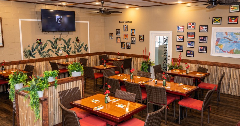 Warm, inviting restaurant interior with wooden tables, red-cushioned chairs, and tropical plants