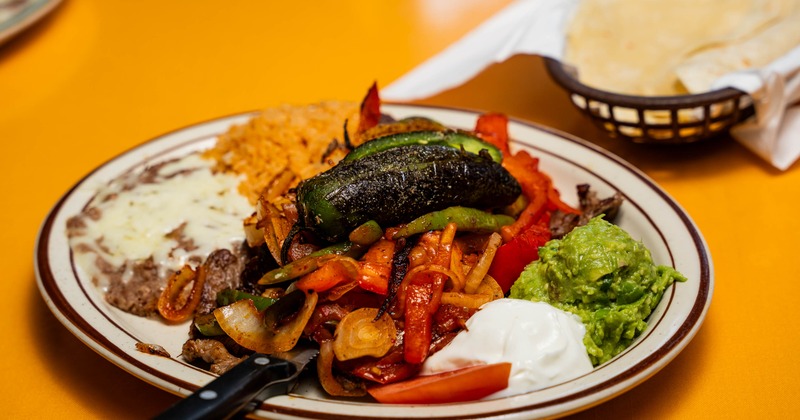 Carne asada with grilled peppers, onions alongside rice, beans, sour cream and guacamole