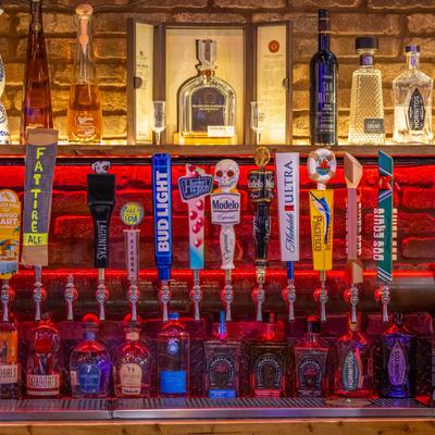 Bar area with draft beer taps with labels and tequila bottles on the shelves.