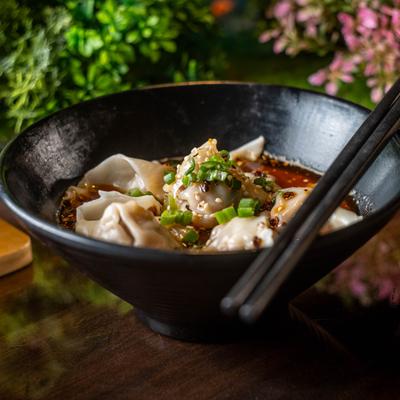 Wontons in spicy broth with chopsticks on a black bowl.