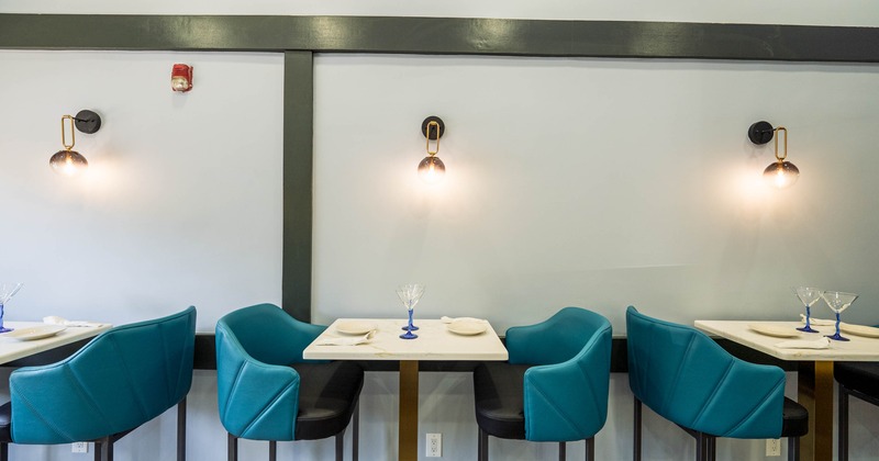 Modern dining area with small square tables, teal chairs, and warm wall sconces