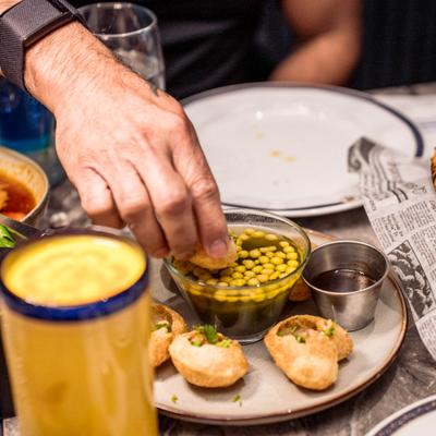 A person enjoying Pani Puri at a table filled with various dishes and Mango Lassi.