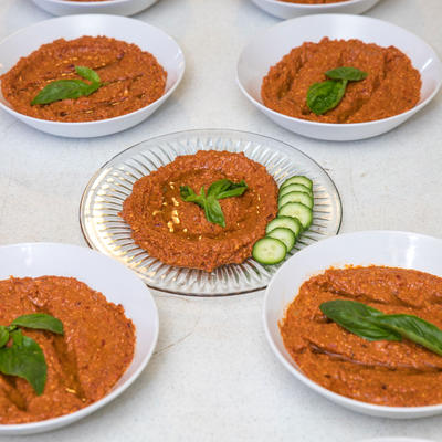Five plates of red sauce with cucumbers