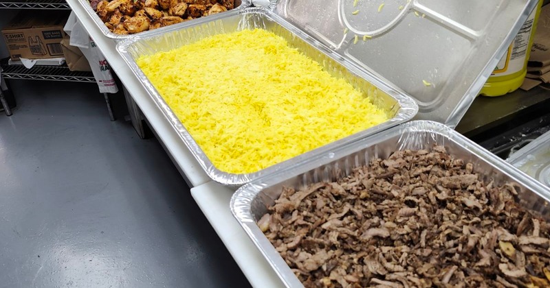 Disposable chaffing dishes with yellow rice and shredded meat on a counter