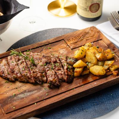 Pluma Iberica steak served on a wooden board with roasted potatoes.
