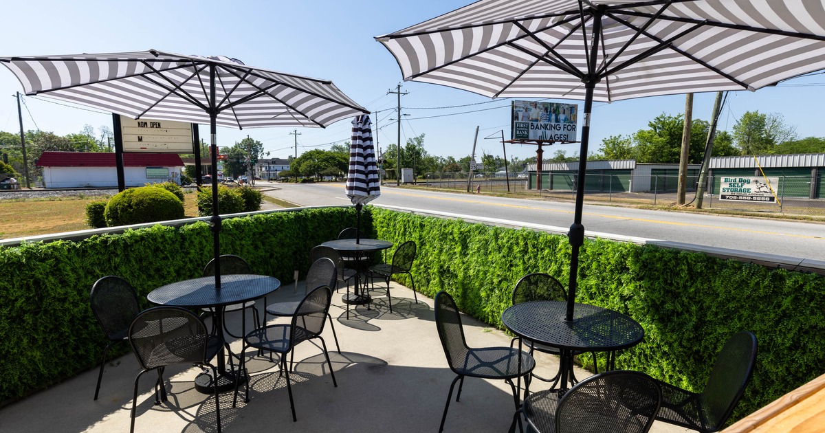 Outdoor seating area - black metal tables and chairs, striped umbrellas, and a green hedge