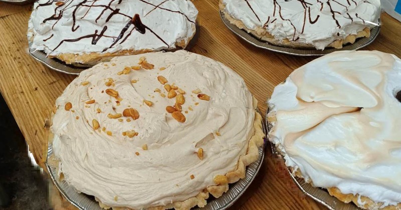 Assorted pies with cream toppings on a wooden table