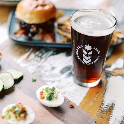 Dark beer in a branded glass beside deviled eggs and a burger.