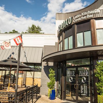Pisco Latin Kitchen features outdoor patio seating and modern curved architecture framing.