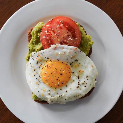 Avocado toast topped with a tomato slice and a fried egg.