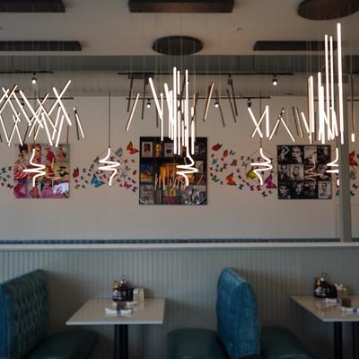 Dining area, hanging tube pendant lights and wall decorated with framed art and butterfly decal.