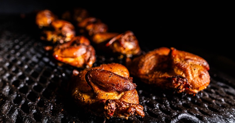 Grilled chicken pieces on a dark, smoky barbecue grill