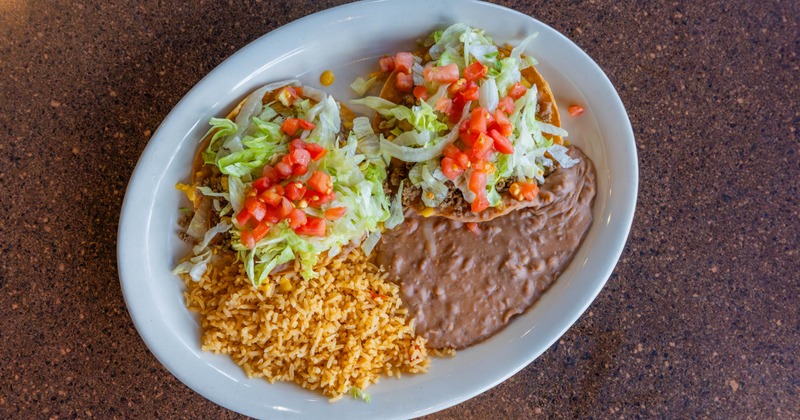 Ground beef tacos, with lettuce, tomato, rice, and refried beans