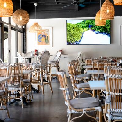 Bright restaurant interior with woven chairs, tables, and rattan pendant lights.