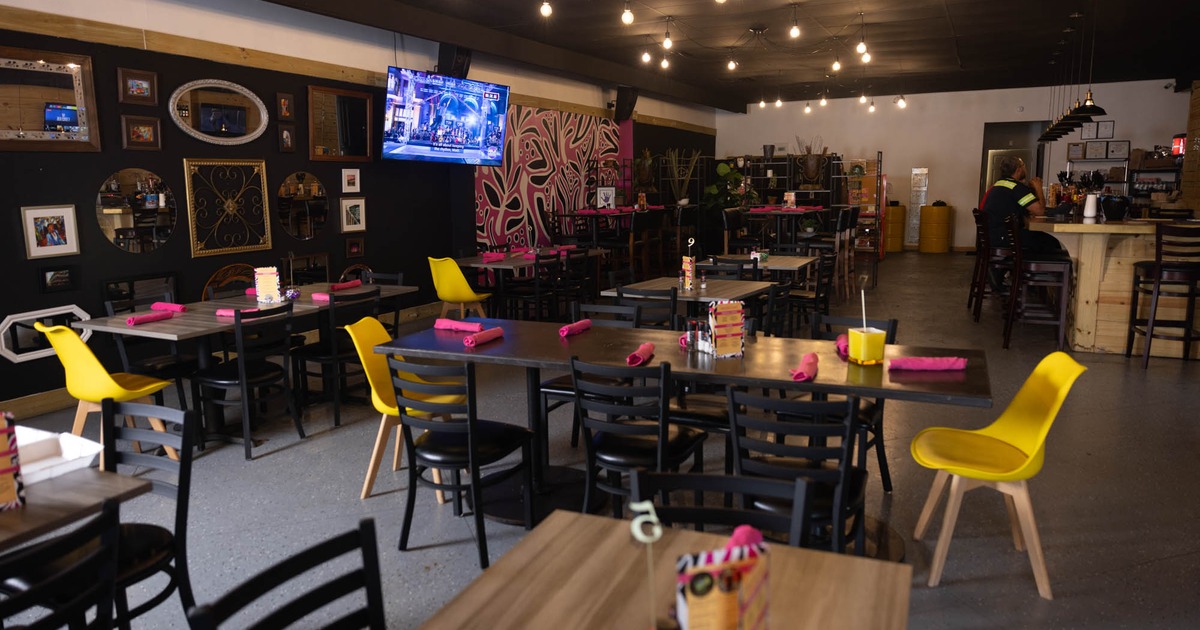 Interior, dark wooden tables, black and yellow chairs, pink napkins, eclectic wall decor