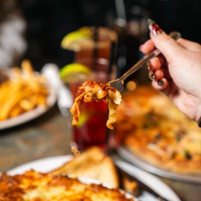 Fork lifting cheesy pasta bite with blurred table food background.